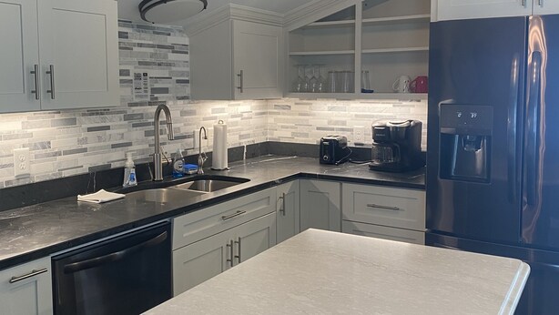 A modern kitchen with white cabinets, a black refrigerator, and a central island. - 4-minute walk to beautiful Emerald Isle beach access. (Emerald Isle)