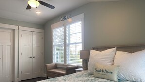 A bedroom with a bed, a ceiling fan, a window with blinds, a nightstand, and a chair. - 4-minute walk to beautiful Emerald Isle beach access. (Emerald Isle)
