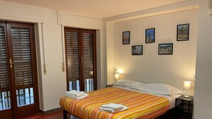 A hotel room with a bed, two bedside lamps, a door with blinds, and four framed pictures on the wall. - Oro Mono (Florence)
