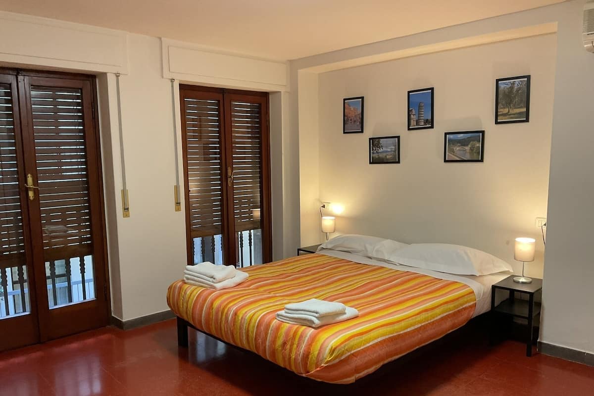 Habitación de hotel con una cama, dos lámparas de noche, una puerta con persianas y cuatro cuadros en la pared.