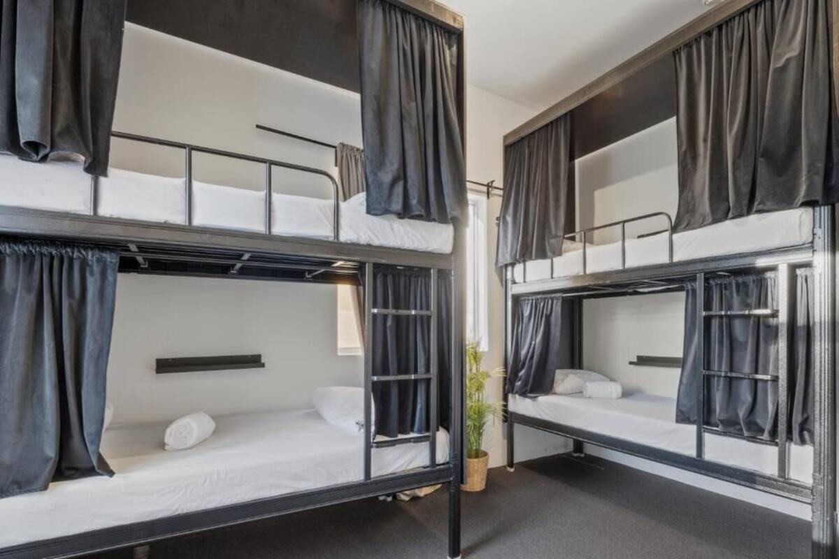 A room with four bunk beds, each with a curtain, a small shelf, and a potted plant.