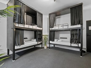 Een kamer met twee stapelbedden, een potplant en een deur met een bordje.