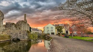 A historic stone building with a large arched window and a chimney, adjacent to a canal with a bridge. - Stunning Modern Christchurch Town Centre Apartment (Christchurch)