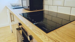 A modern kitchen with a black induction cooktop, a microwave, and a stainless steel kettle on a wooden countertop. - Stunning Modern Christchurch Town Centre Apartment (Christchurch)