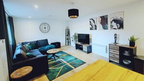 A modern living room with a sofa, coffee table, TV, and artwork on the walls. - Stunning Modern Christchurch Town Centre Apartment (Christchurch)