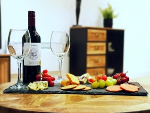 A wine bottle, two glasses, and a cheese board with various cheeses and fruits on a wooden table. - Stunning Modern Christchurch Town Centre Apartment (Christchurch)