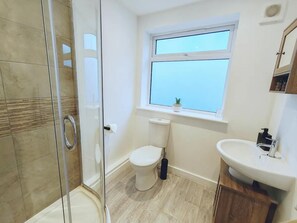 A modern bathroom with a glass shower enclosure, a toilet, and a sink with a window above. - Stunning Modern Christchurch Town Centre Apartment (Christchurch)