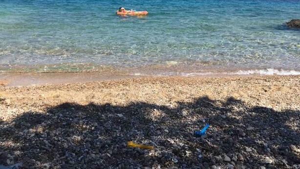 Una spiaggia con acque cristalline, una persona che galleggia su un’isola e montagne in lontananza.