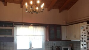 Una cucina con travi in legno, un lampadario, pensili bianchi, una finestra con tende, un forno a microonde e un frigorifero.