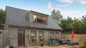 A wooden house with a sloped roof, a front door, and windows. There is a gravel patio with outdoor furniture and potted plants.
