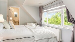 A bedroom with a bed, a window with curtains, a radiator, and a bathroom visible through an open door.
