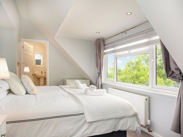 A bedroom with a bed, a window with curtains, a radiator, and a bathroom visible through an open door.