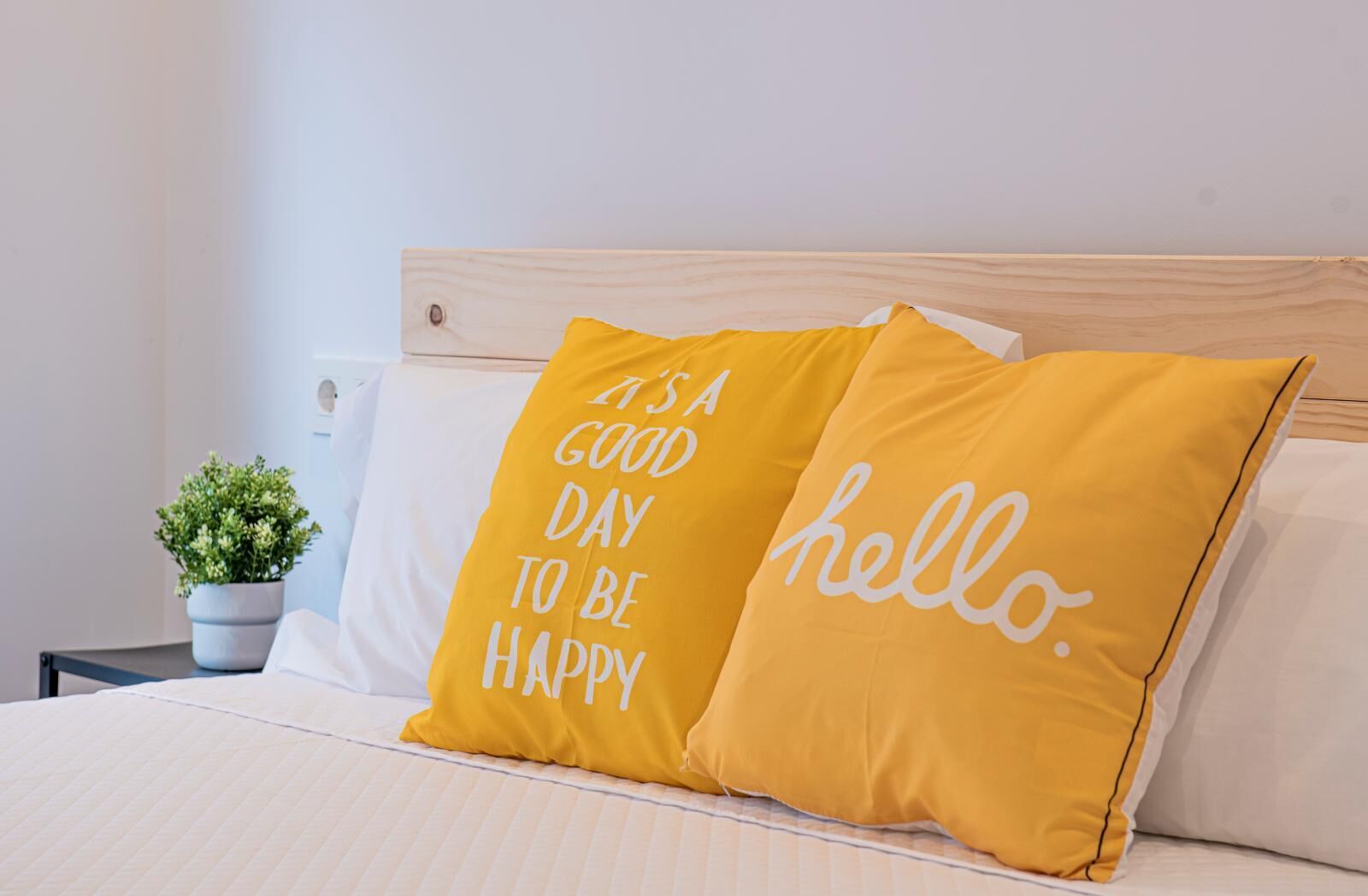 Una cama con dos almohadas, una con la frase 'Es un buen día para ser feliz' y la otra con la palabra 'hola'.