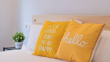 Una cama con dos almohadas, una con la frase 'Es un buen día para ser feliz' y la otra con la palabra 'hola'.