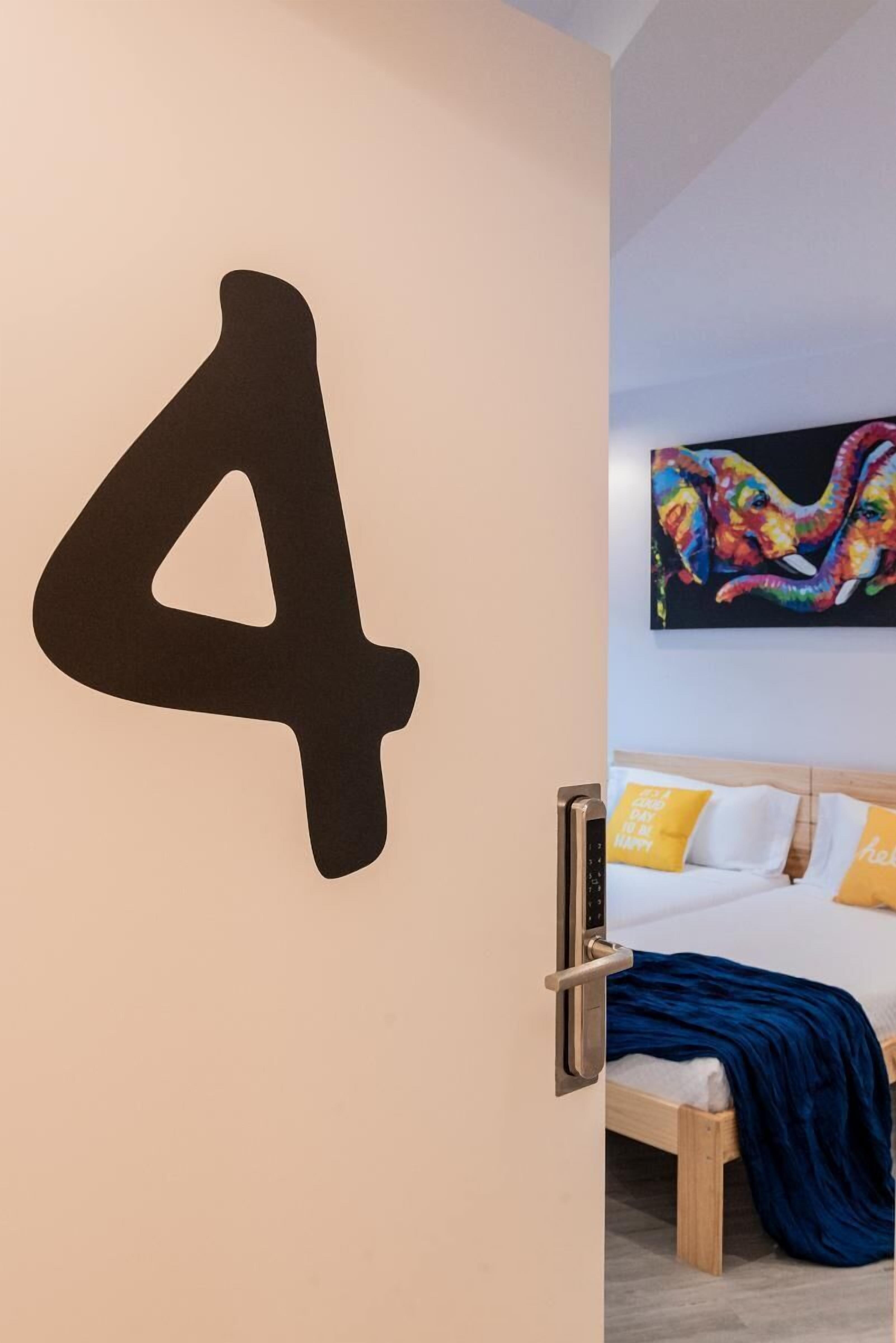 A room with a bed, a door with a large number 4, and a colorful artwork above the bed.