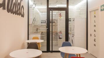 A modern interior with a glass door labeled "Cocina Kitchen" and "Almacén" on the right. There are three round tables and chairs in the room.