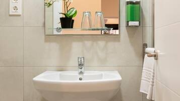 Un baño con un lavamanos blanco, un espejo y una orquídea en maceta.