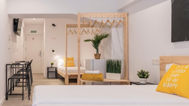 A hotel room with a bed, a desk, a chair, a hanging clothes rack, and a potted plant. - Bilbao ROOMS & KITCHEN Zorroza (Bilbao)