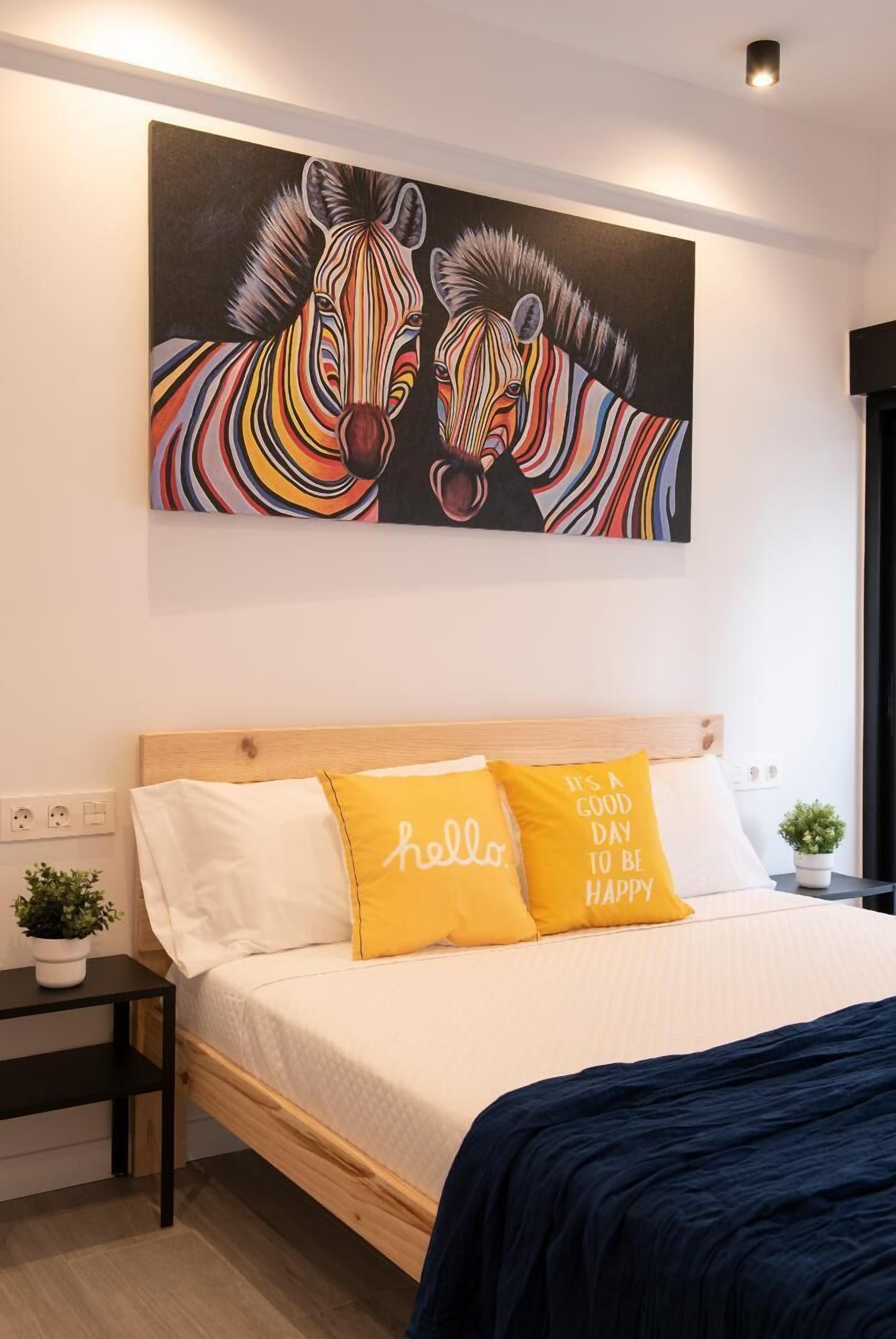 Un dormitorio con una cama, dos almohadas, una mesita de noche, una planta pequeña y un cuadro de cebra en la pared.