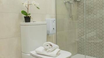Un baño moderno con inodoro, cabina de ducha de vidrio y una orquídea en maceta.