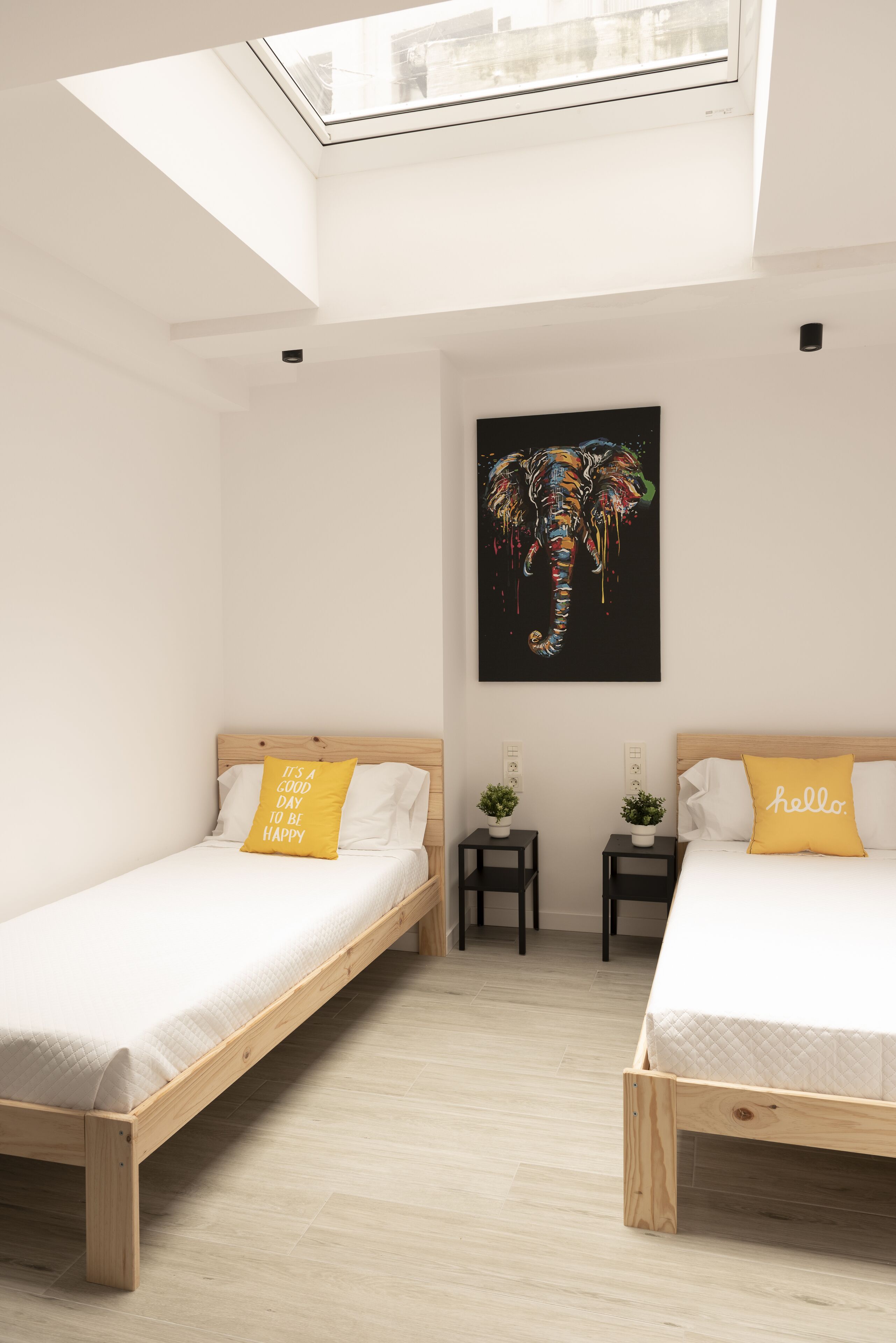 Een moderne hotelkamer met twee enkele bedden, een dakraam, een kunstwerk van een zwarte olifant en kleine potplanten.