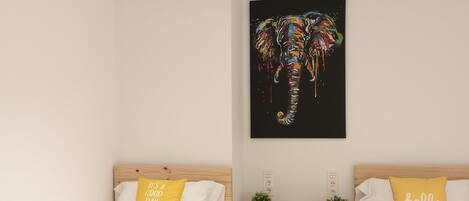 Quarto de hotel moderno com duas camas de solteiro, um claraboia, uma obra de arte de elefante preto e pequenas plantas em vasos.