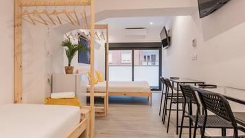 A modern hotel room with two beds, a dining area, and a TV mounted on the wall.