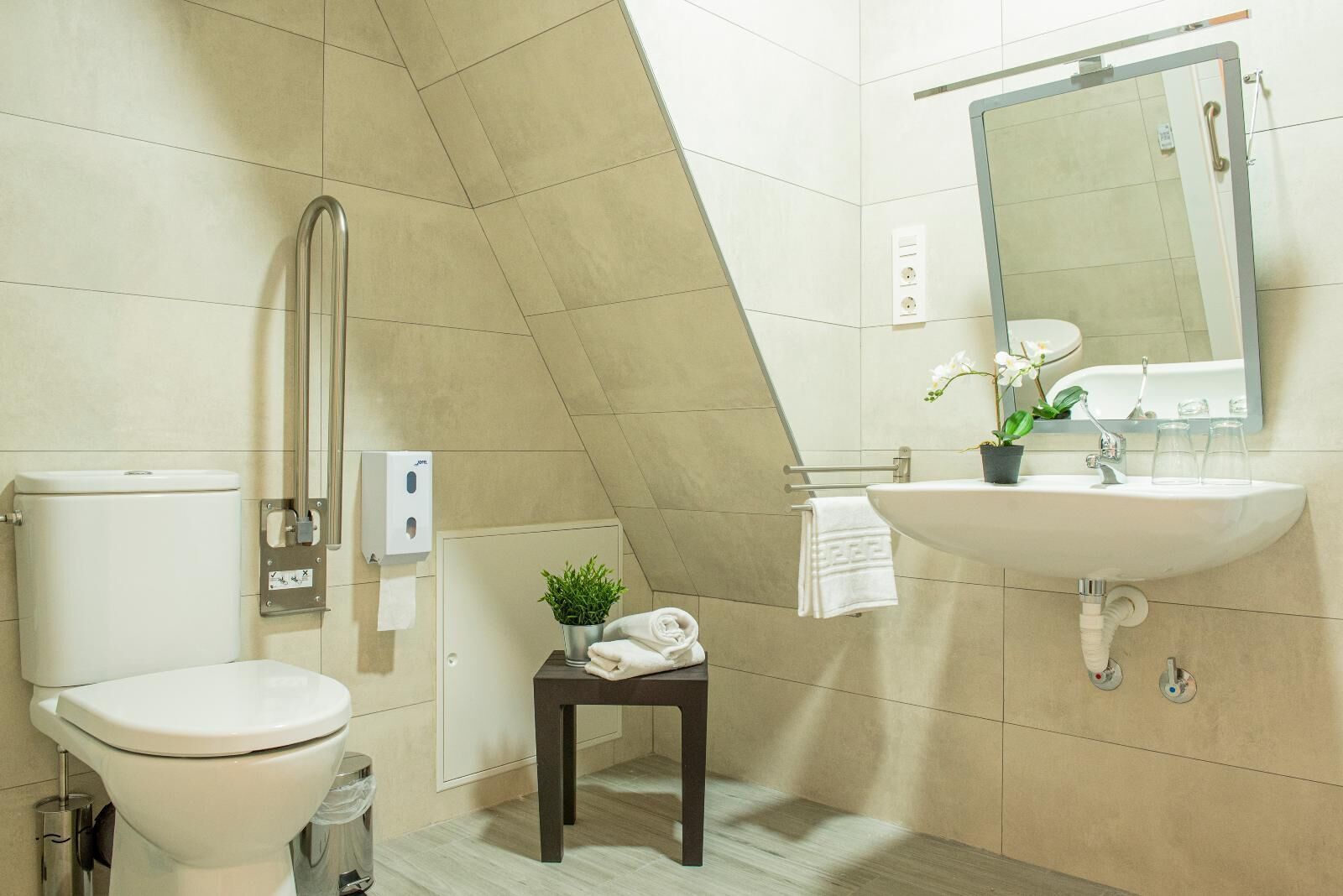 Une salle de bain moderne équipée de toilettes, d’un bidet, d’un lavabo et d’une petite table agrémentée d’une plante et de serviettes.