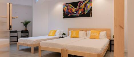 Una habitación de hotel moderna con dos camas de madera, un cuadro abstracto grande y un almohadón amarillo brillante con un mensaje optimista.
