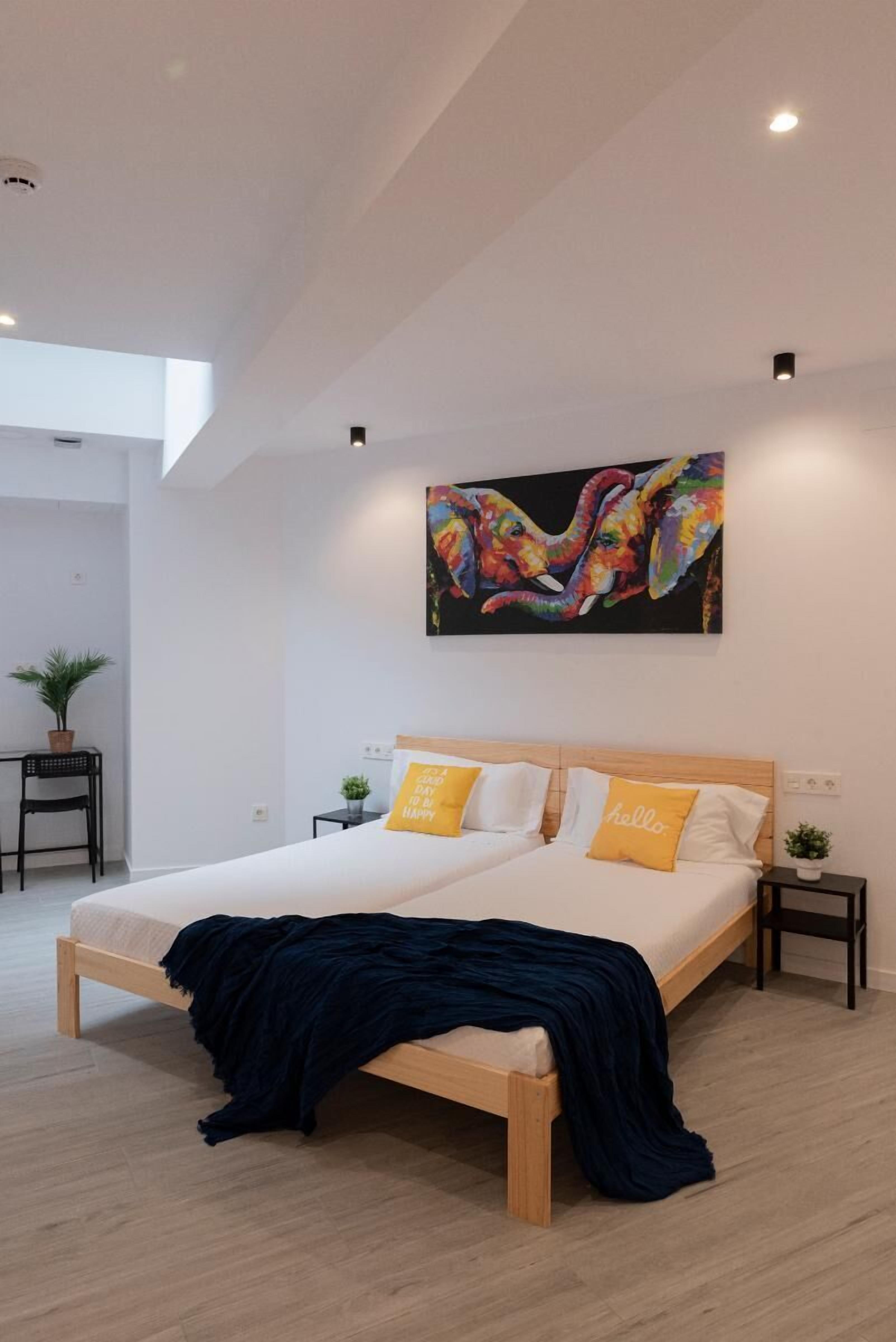 A modern bedroom with a large bed, a colorful painting above it, and a skylight.