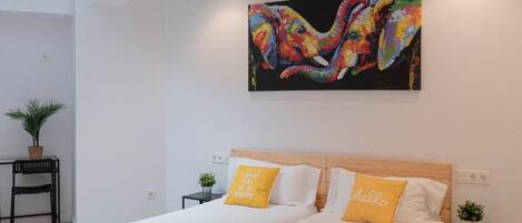 A modern bedroom with a large bed, a colorful painting above it, and a skylight.