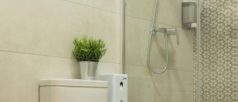 Un baño moderno con inodoro, cabina de ducha de vidrio y una pequeña planta en el tanque.