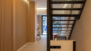 A modern interior with a wooden panel wall, a staircase with a mesh design, and a reception desk. - Bilbao ROOMS & KITCHEN Zorroza (Bilbao)