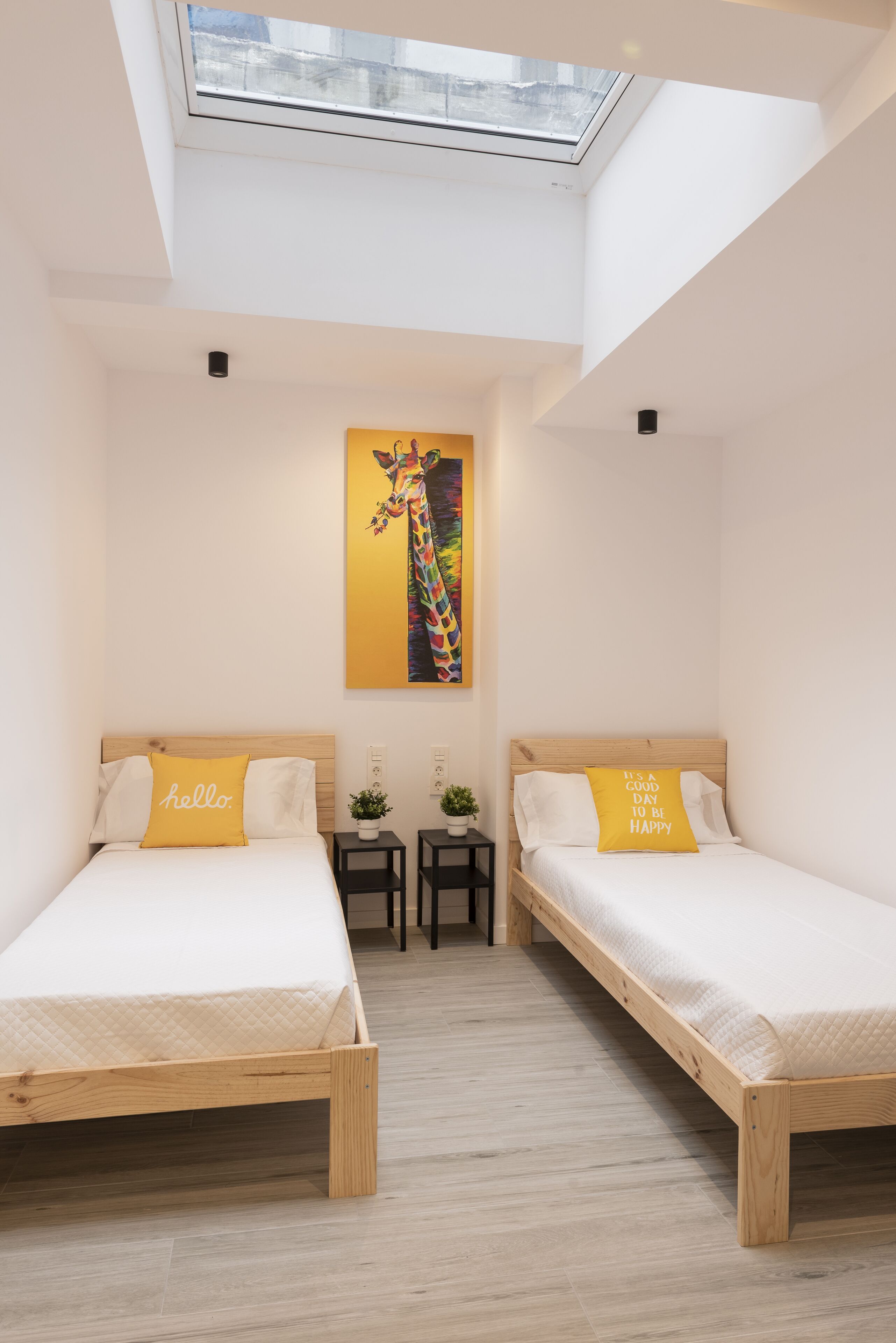 Ein Zimmer mit zwei Holzbett, einem Oberlicht, einem Giraffenbild und zwei kleinen Tischen mit Pflanzen.