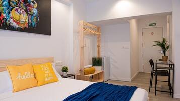 Una camera d'albergo moderna con un letto, un quadro, una rastrelliera in legno per abiti, un piccolo tavolo con una pianta e una scrivania con una sedia.