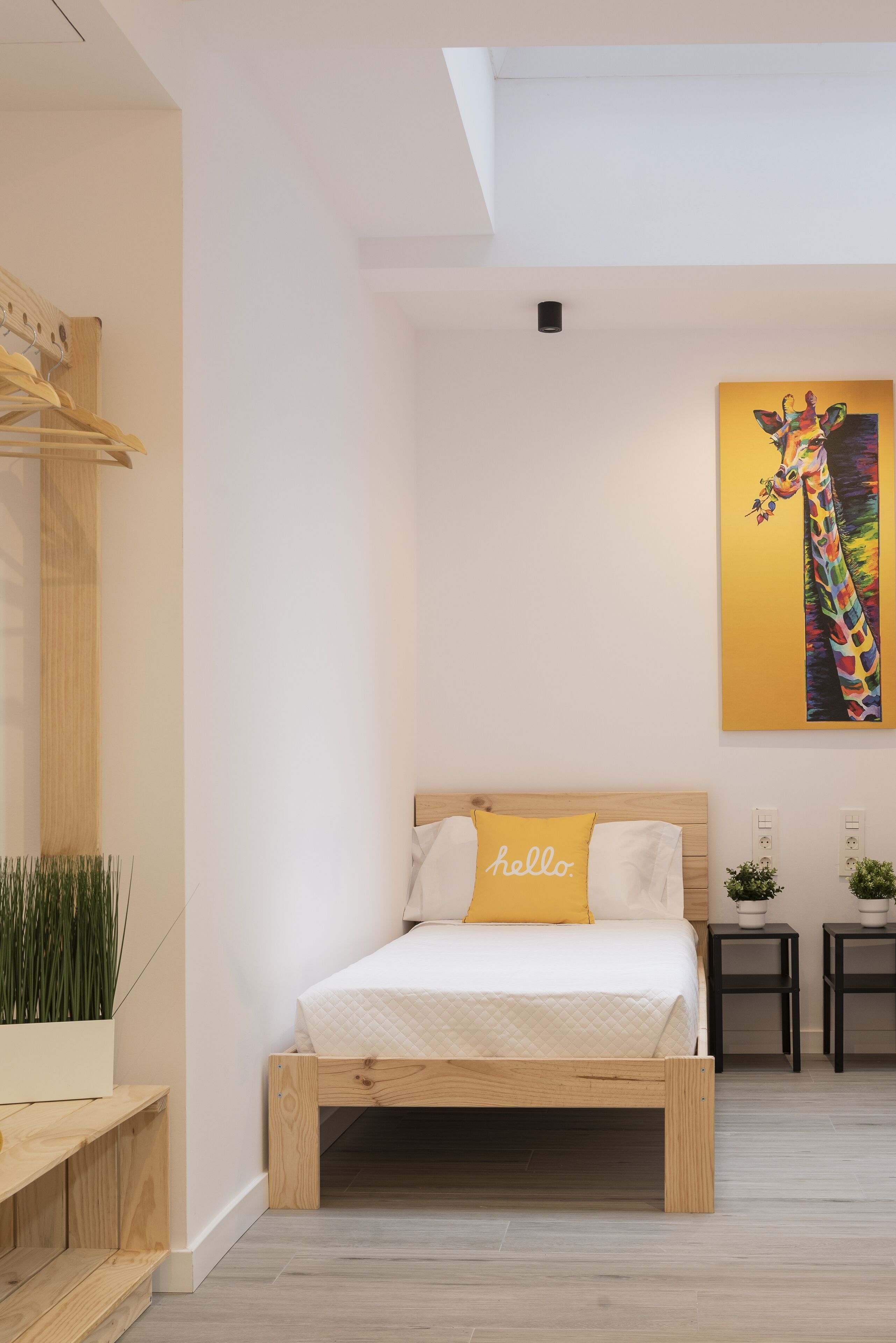 A modern bedroom with a wooden bed, a yellow pillow, a wall-mounted painting, and a skylight.