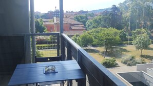 A balcony with a table and chairs, overlooking a courtyard with trees and buildings.