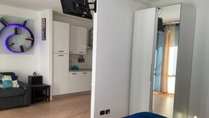 A modern bedroom with a bed, a TV mounted on the wall, a kitchen area, and a bathroom with patterned curtains.