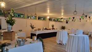 A spacious indoor venue with multiple round tables covered with white tablecloths, wooden flooring, and hanging light fixtures. - Gite - 800 m from the sea & commodities in a parc of  3,5ha for familly event -  (Loctudy)