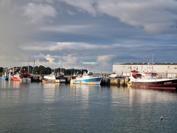 A harbor with several boats docked, a large building in the background, and a calm water surface.