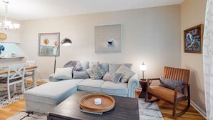 Una sala de estar con un sofá azul claro, una mesa de centro de madera y una alfombra estampada.