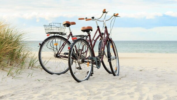 Dos bicicletas estacionadas en una playa arenosa, con el océano al fondo.