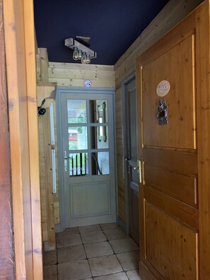 A wooden door with a glass panel and a number plate, a hallway with wooden walls, and a ceiling light fixture. - Chalet le Chamois, Apartment 10—right at the slopes (Bourg-Saint-Maurice)