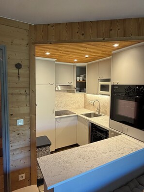 A compact kitchen with white cabinetry, a granite countertop, and a built-in oven.