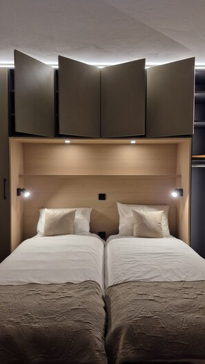 A hotel room with a double bed, two bedside tables, a headboard with integrated lighting, and a wall-mounted TV.