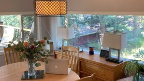 A dining area with a wooden table, chairs, a laptop, a vase with flowers, and a view of greenery outside. - History and Romance abound in this restored home & cabin in cozy Evergreen (Evergreen)