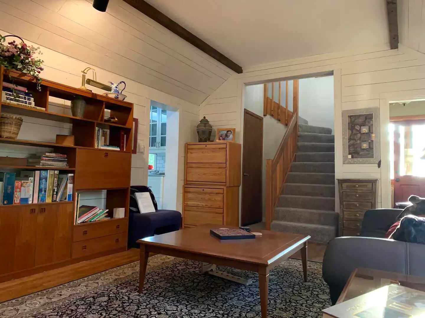 A cozy living room with a wooden bookshelf, a blue sofa, a coffee table, and a staircase leading to another level.