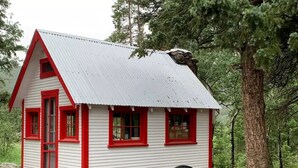 A small, white building with red trim and windows, surrounded by trees and a wooden cart. - History and Romance abound in this restored home & cabin in cozy Evergreen (Evergreen)