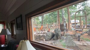A room with a large window overlooking a rustic outdoor area with wooden structures and rocks. - History and Romance abound in this restored home & cabin in cozy Evergreen (Evergreen)