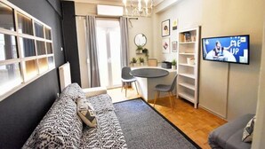 A modern living room with a sofa, a dining table with chairs, a TV, and a bookshelf. - Seven Seconds Away (Athens)